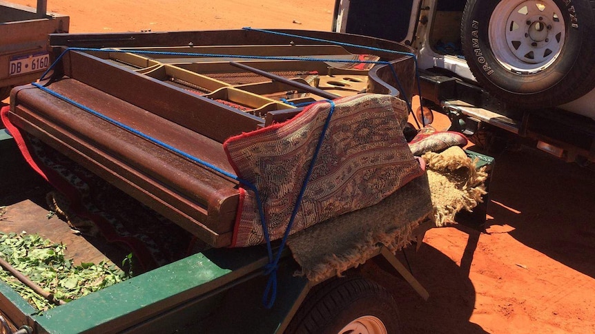 A photo of the piano wrapped in carpet and placed on the back of a trailer.