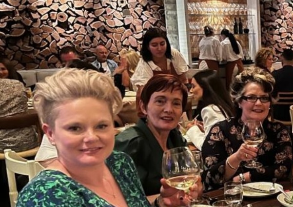 Roxanne, Gail and Angela sit in an expensive-looking restaurant, raising glasses and smiling.