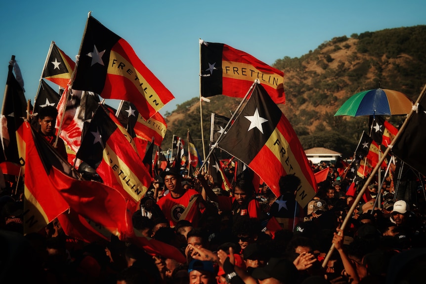 Red, black and yellow flags waved in the air by young Timorese at a Fretelin rally on a sunny day