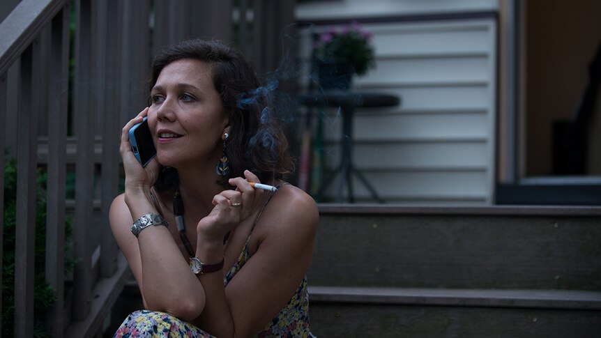 Colour close-up still of Maggie Gyllenhaal talking on phone and smoking on porch steps in 2018 film The Kindergarten Teacher.