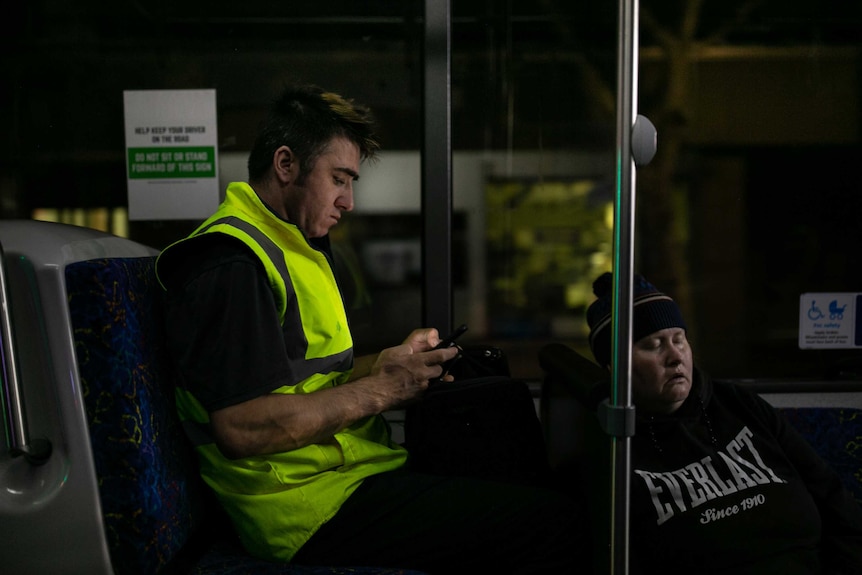 A man sits on a bus looking at his phone.