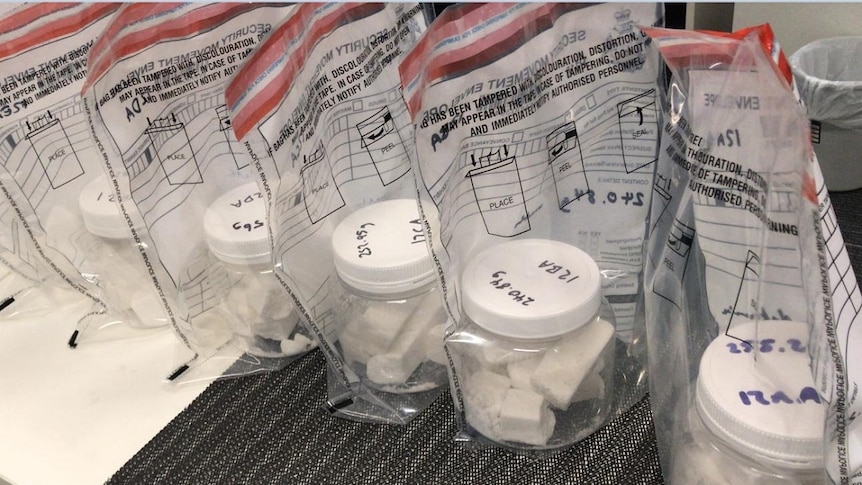 Jars of methamphetamine, a white substance, in jars which are in zip lock bags, sitting on a table in a row.