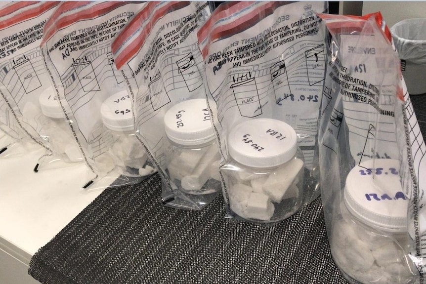 Jars of methamphetamine, a white substance, in jars which are in zip lock bags, sitting on a table in a row.