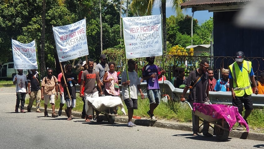 Young PNG nationals push wheelbarrow collecting cash donations and wave placards in support of Australian bushfire victims