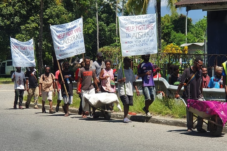 Young PNG nationals push wheelbarrow collecting cash donations and wave placards in support of Australian bushfire victims