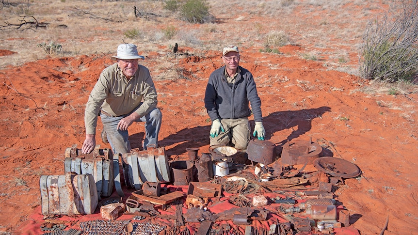 Two men crouching down in desert sitting with equipment from early explorer