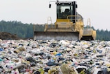Heavy machinery scooping up rubbish at a landfill site.