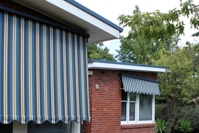 Striped outside canvas blinds covering windows of red brick house.
