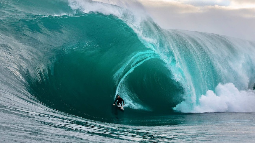 A surfer pulls into a huge, glassy barrel.