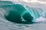 A surfer pulls into a huge, glassy barrel.