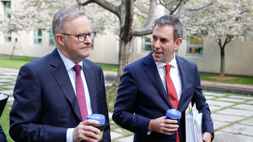 Jim Chalmers and Anthony Albanese walk in a court yard at parliament house with coffees