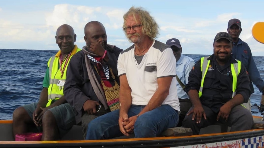 Tony McCracken, in a t-shirt and jeans, sits aboard a small rescue vessel with rescue team of five as he is taken back to shore.