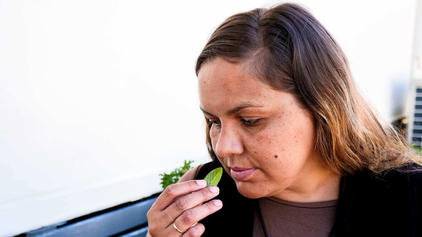A woman smelling a chocolate mint leaf sitting down.