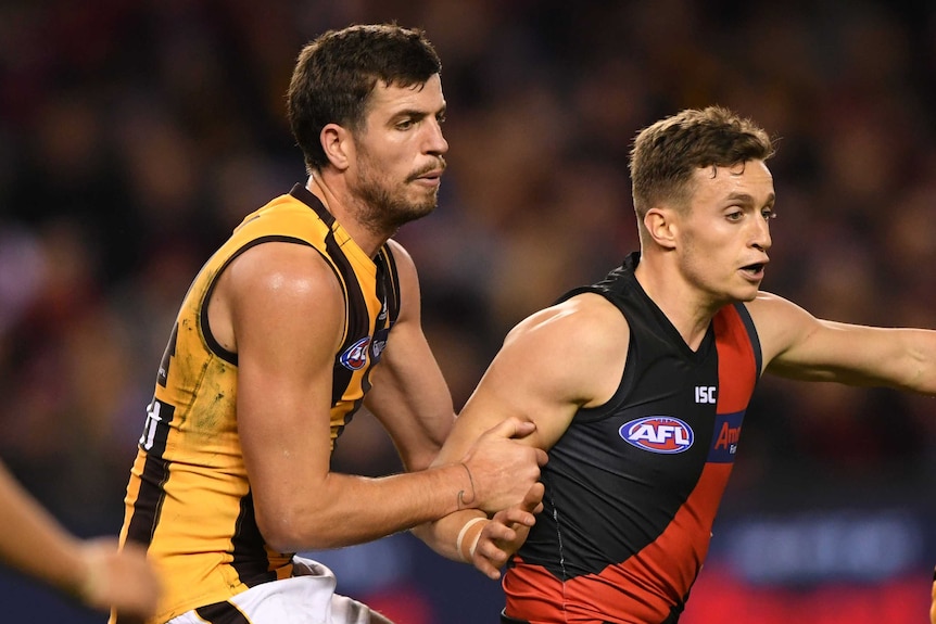 An AFL player holds onto the right arm of an opponent with both hands.