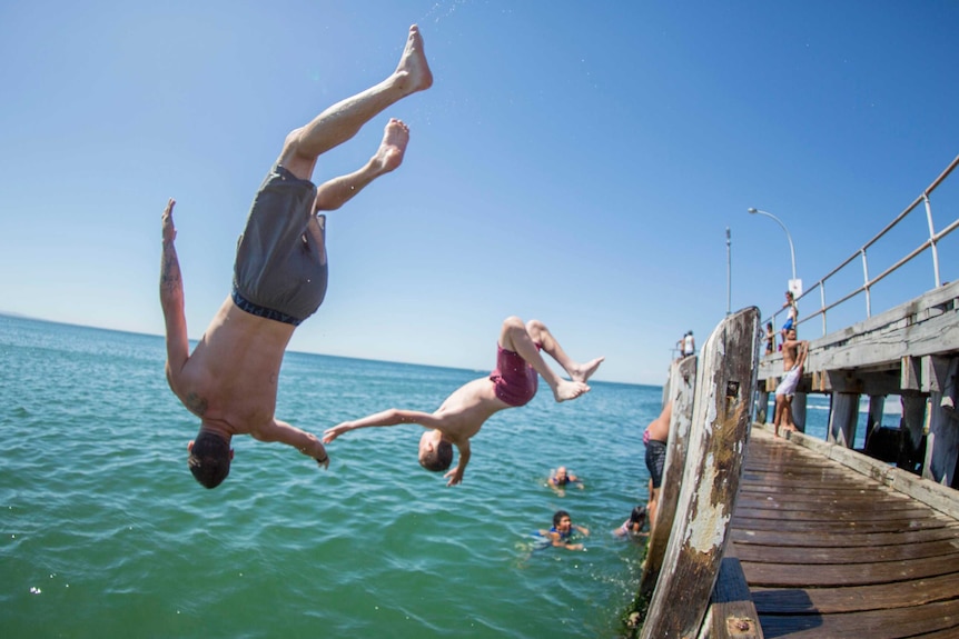 Two young men backflip of a pier