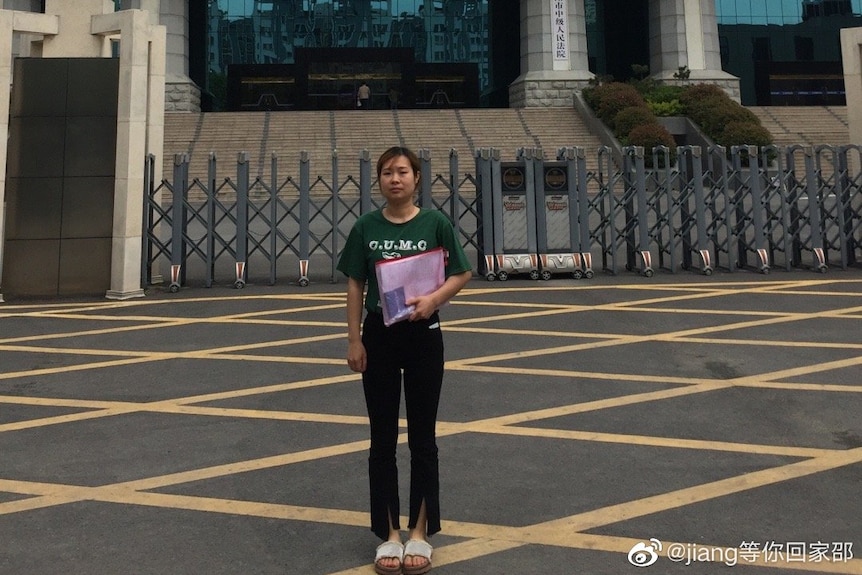 Jiang's wife Shao Fen stands outside the courtroom with files in her arms.