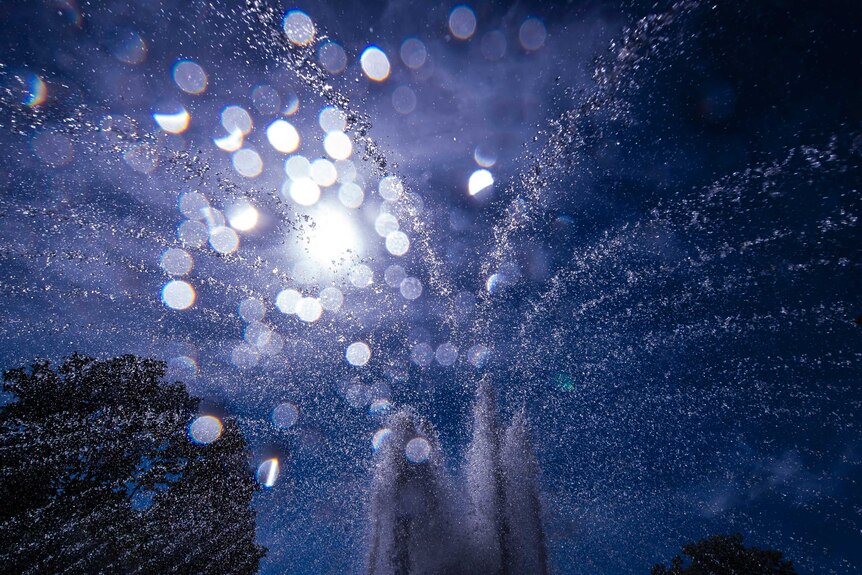Water drops of a fountain fall on the lens in front of the sun.