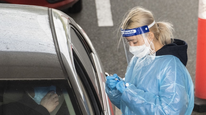 A woman wearing protective gear stands next to a car