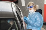 A woman wearing protective gear stands next to a car