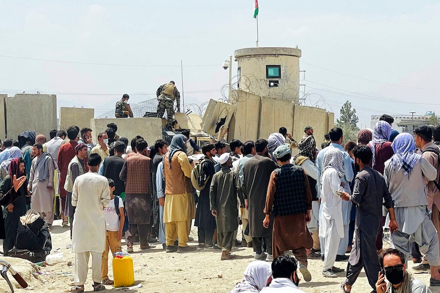 Afghan security guards stand on a wall as hundreds of people gather outside the international airport in Kabul.