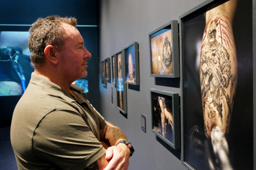 A man looks at a framed photograph of a tattoo.