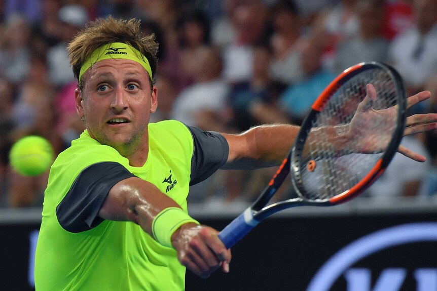 Tennys Sandgren in fluro green kit focusses on the ball and has his racquet out
