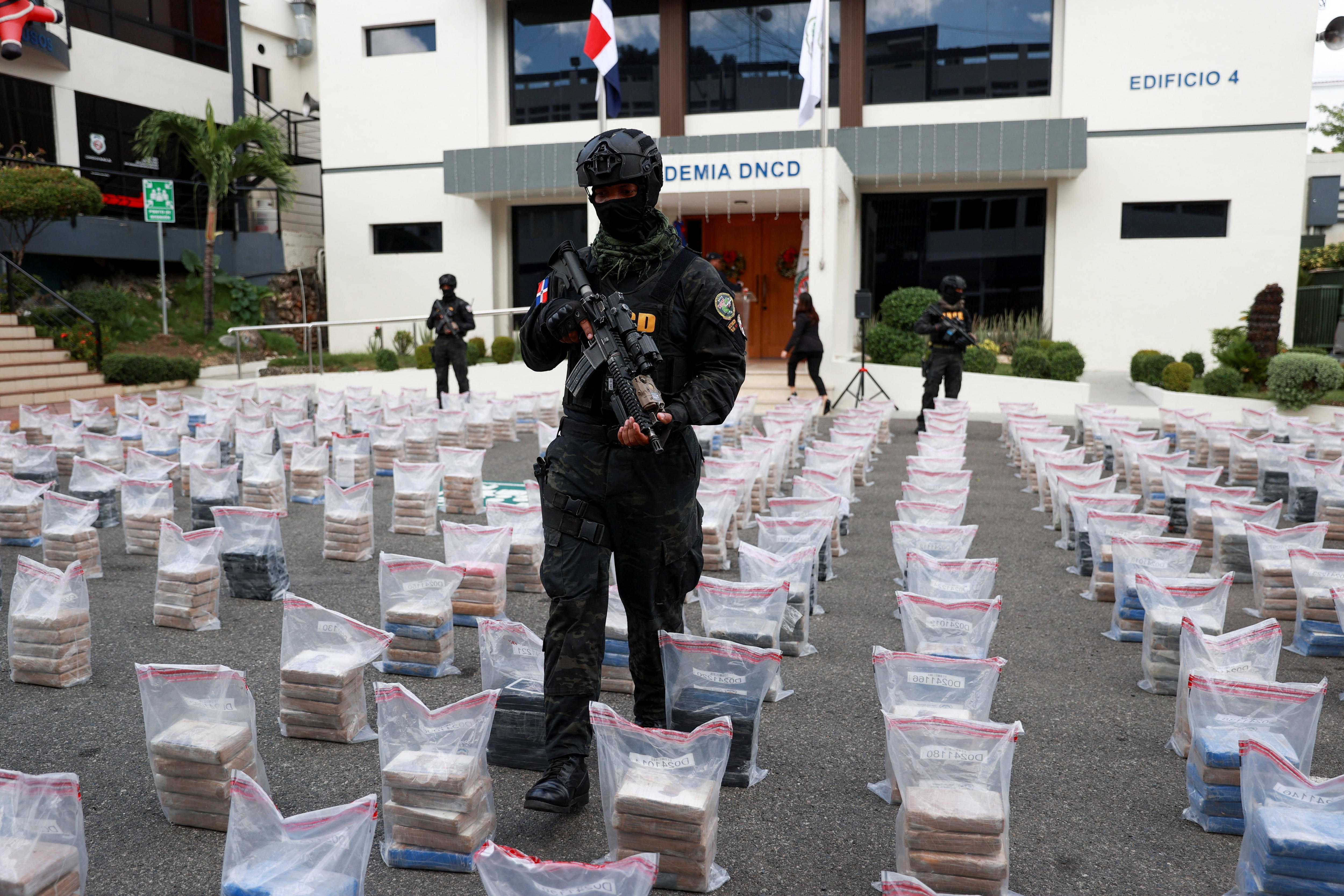 Hombres armados con uniformes negros forman filas sobre bolsas llenas de paquetes. 