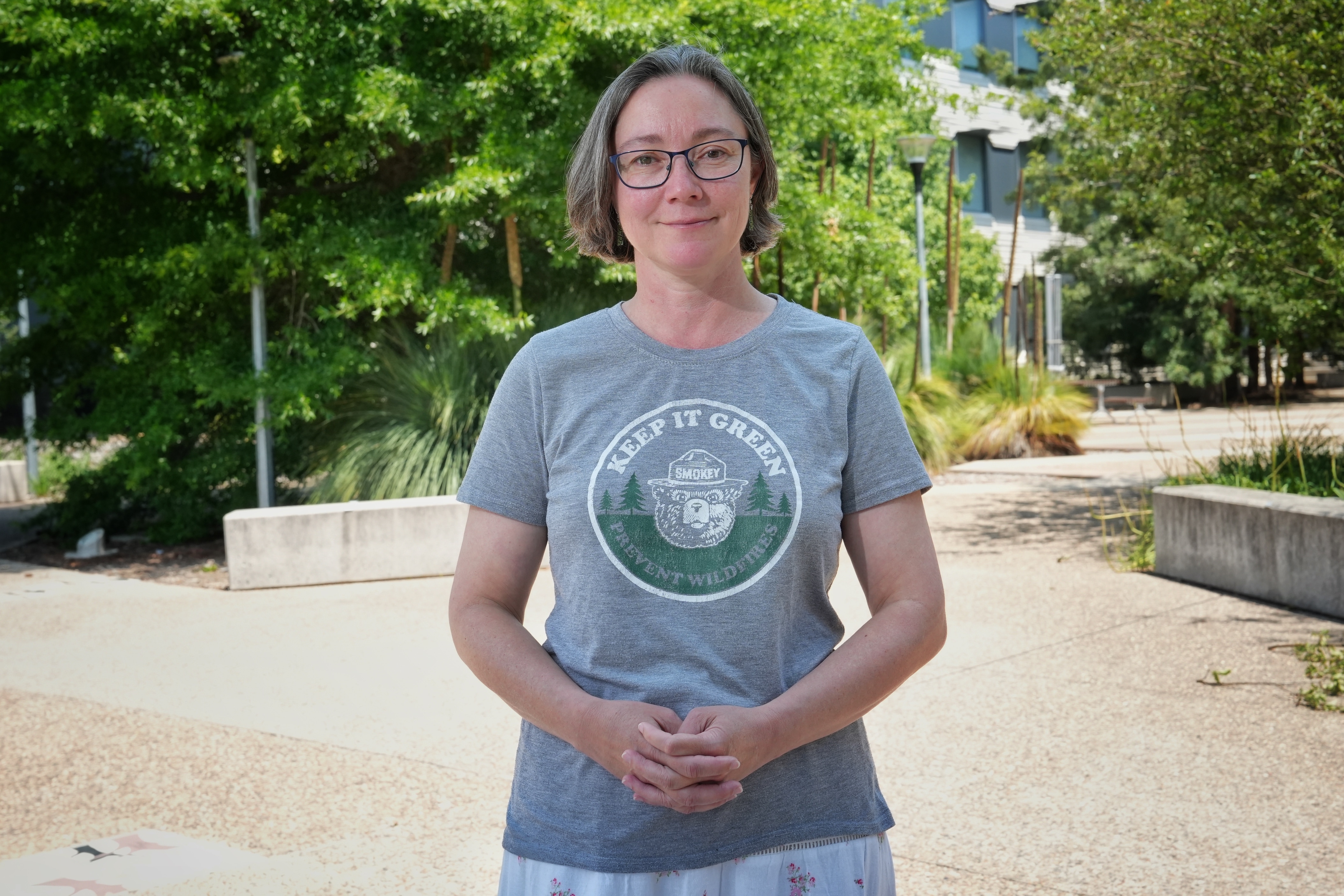Una mujer con pelo corto y gafas está afuera sonriendo.