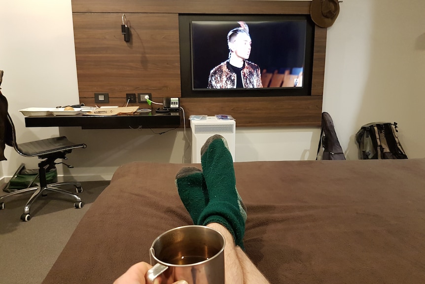 Feet up on bed, TV on in hotel room