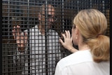 Woman tries to touch a man's hand through the bars of a prison.