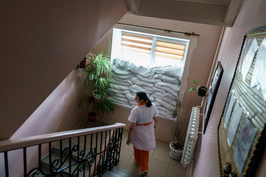 Sandbags are piled against a window inside the Pokrovsk Perinatal Hospital, woman staff in uniform walks downstairs down stairs