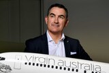 Virgin Australia boss Paul Scurrah looks off to the right while standing behind a model plane.