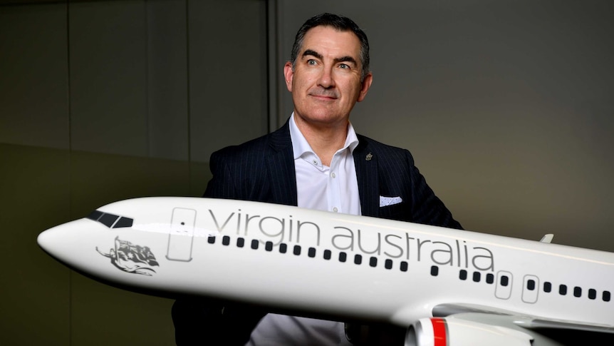 Virgin Australia boss Paul Scurrah looks off to the right while standing behind a model plane.