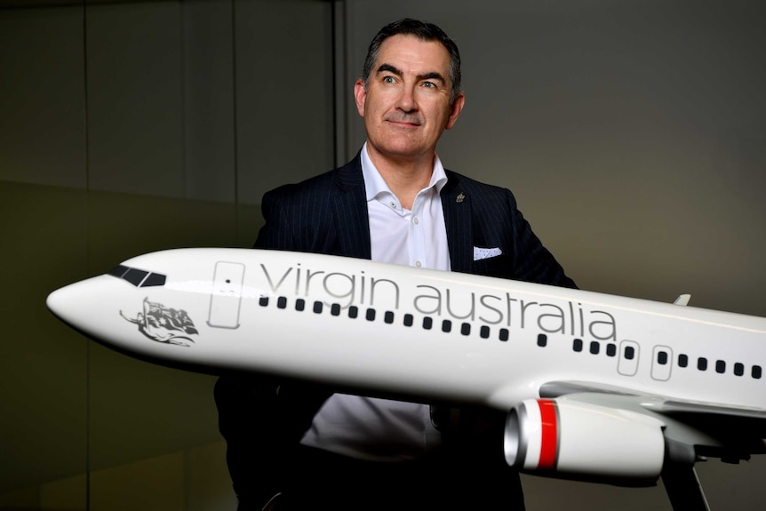 Virgin Australia boss Paul Scurrah looks off to the right while standing behind a model plane.