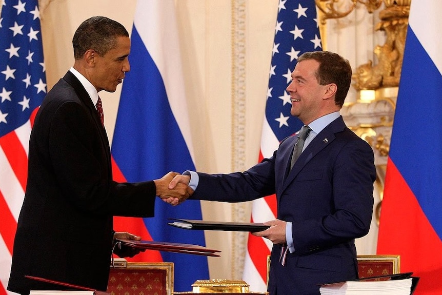 Obama and Medvedev shake hands in front of a backdrop of Russian and US flags