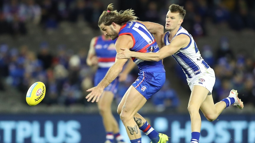 A Western Bulldogs AFL player is tackled by a North Melbourne opponent around his arms.