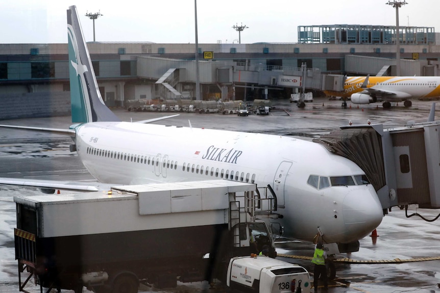 A SilkAir aircraft is parked at an airport gate with the gangway down.
