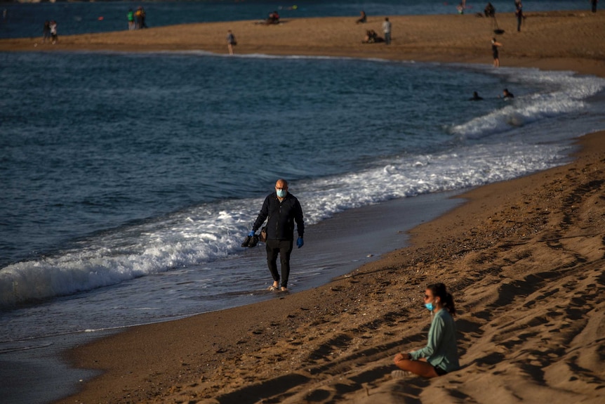 People sit and walk in a beach in Barcelona