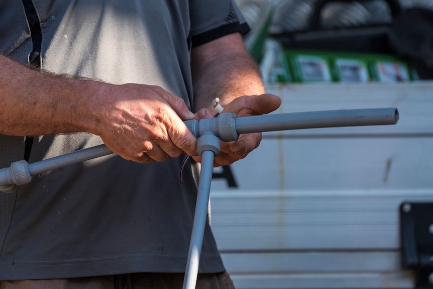 Man in grey shirt holding a grey plastic pipe