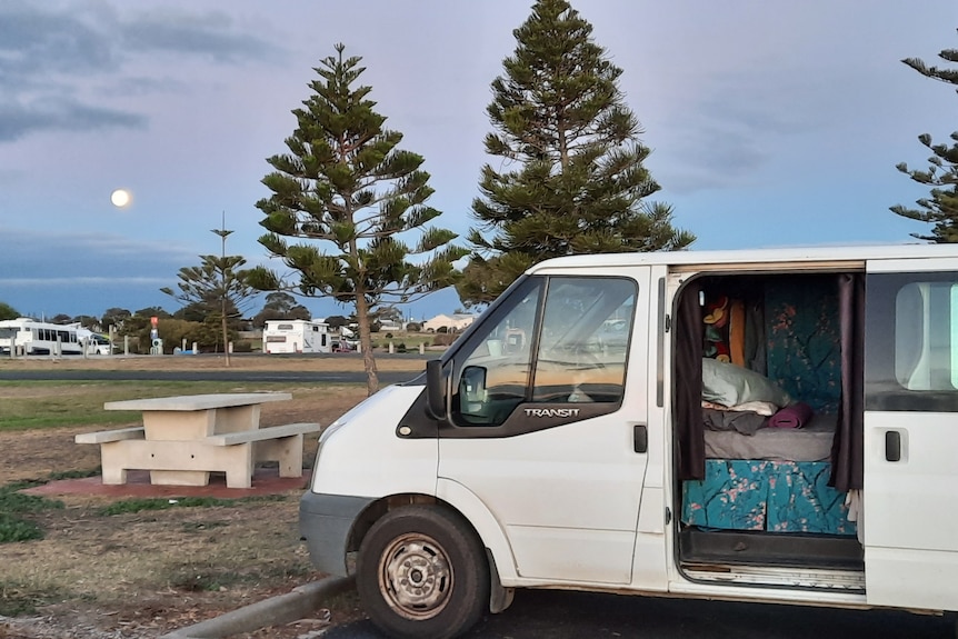 Van with a mattress inside parked at a park during sunset.