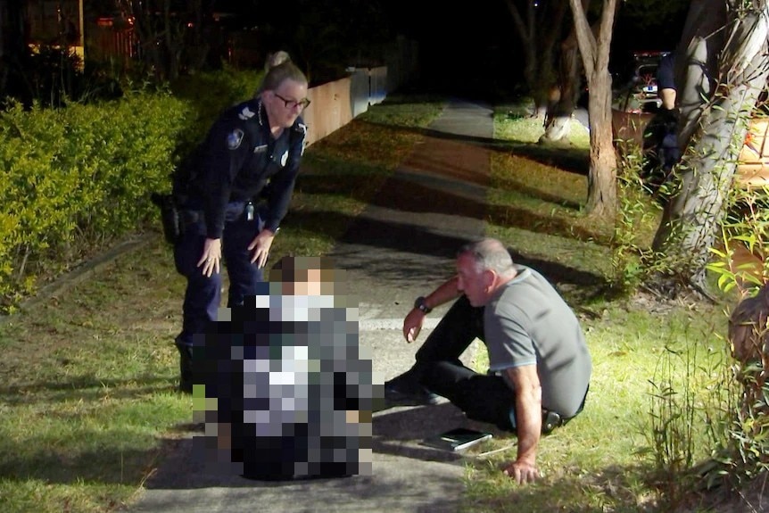 man and woman speak to teenager sitting on footpath.