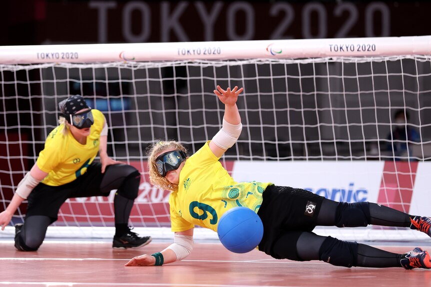 Australian goalball player Brodie Benson is horizontal, trying to stop the ball from getting in the goal.