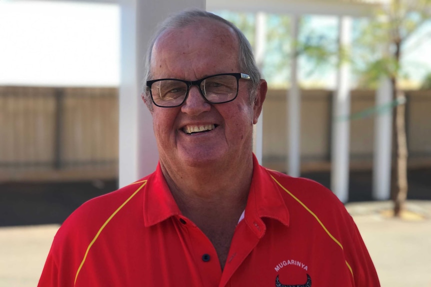 Bespectacled man in r red shirt smiles into camera