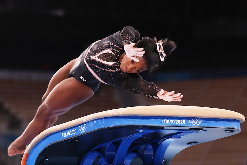 Simone Biles twists her body in mid-air as she reaches her hands out to plant on the vault in Olympic training.