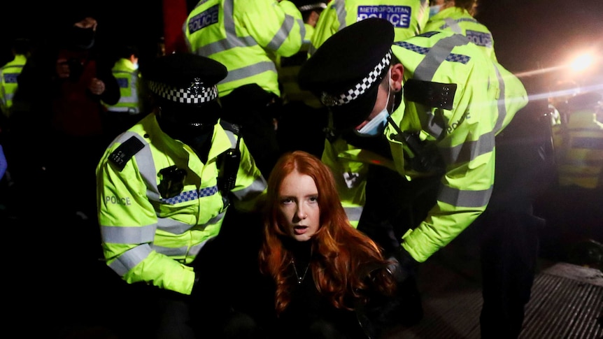 Police put handcuffs on a woman looking at the camera.