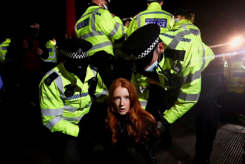 Police put handcuffs on a woman looking at the camera.