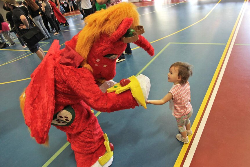 A woman wearing a furry red horse suit shakes hands with a small child