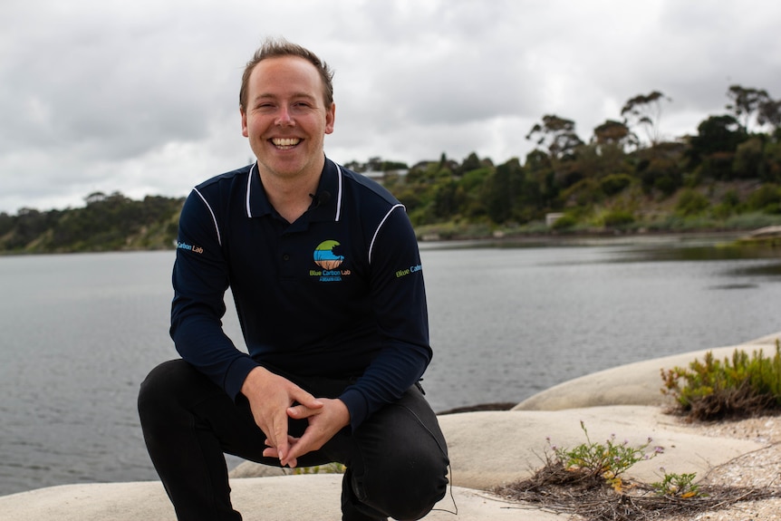 Paul Carnell crouches with the ocean behind him on a grey day.