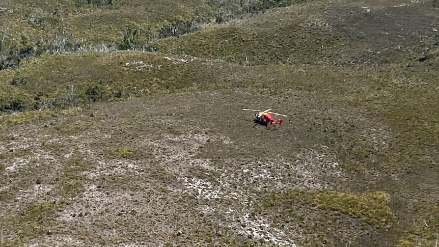 A rescue helicopter is seen flying over mountainous terrain.