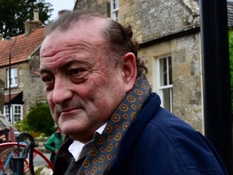 An old man standing next to a British house. 